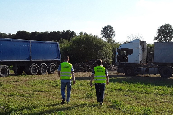 Inspektorzy ochrony środowiska na tle ciężarówek stojących na polu