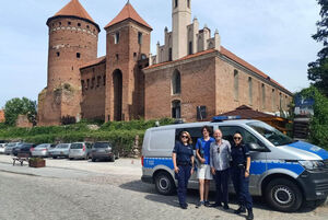 Policjantki w towarzystwie mężczyzny i jego syna. Wszyscy stoją przy radiowozie ustawionym na tle zamku