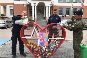 Policjanci i żołnierz wrzucają nakrętki do pojemnika