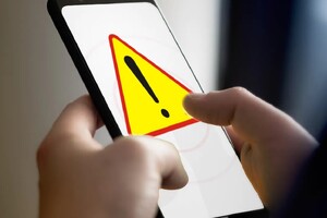 Dłoń trzymająca smartfon wyświetlający znak UWAGA na ekranie