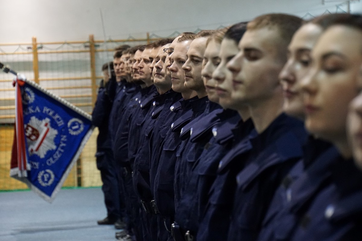 Policjanci stojący w szeregu i sztandar KWP w Olsztynie w tle