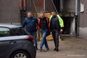 Zatrzymany mężczyzna prowadzony przez policjantów do radiowozu