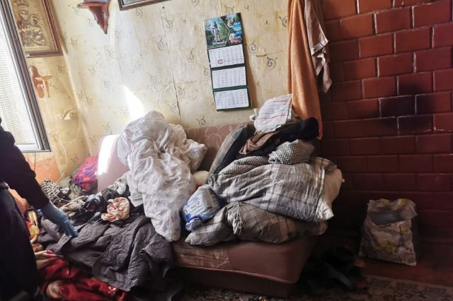 Pokój w mieszkaniu seniorki przed interwencją wolontariuszy. Ogólny bałagan, śmieci porozrzucane po podłodze,