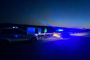 Radiowozy i zatrzymany bus stojące na poboczu drogi. W centralnym punkcie widoczni są policjanci