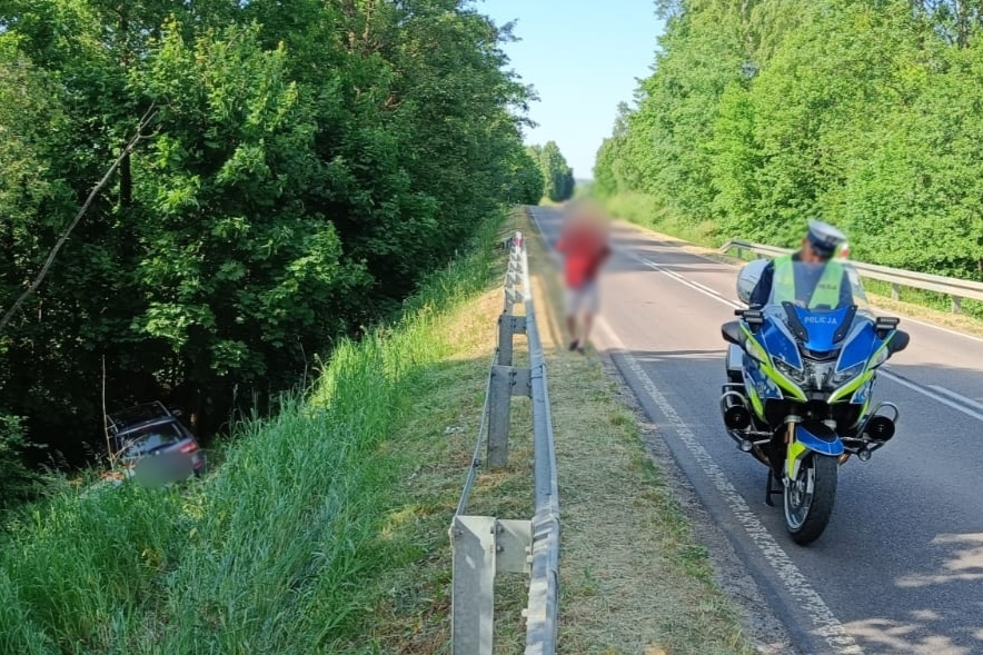 Policyjny motocykl na drodze i samochód w zaroślach