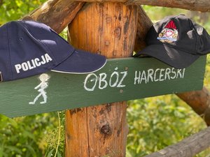 Policyjna i strażacka czapki leżące na drogowskazie do obozu