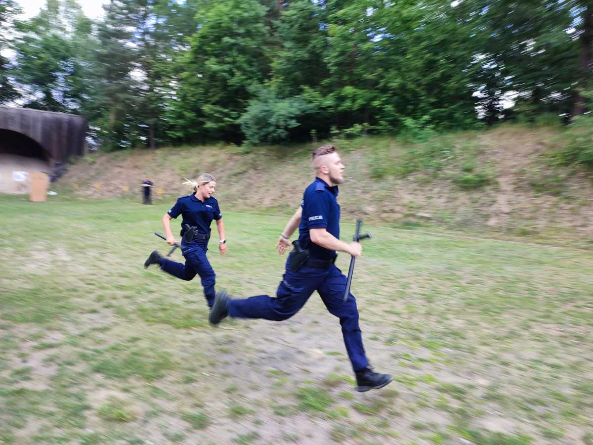 Uczestnicy zawodów podczas konkurencji tor przeszkód. Dwoje biegnących policjantów