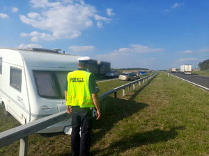 Policjant stojący przy przyczepie kempingowej rozbitej o barierę ochronną