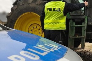 Policjant podczas kontroli ciągnika rolniczego, stojący między radiowozem a traktorem