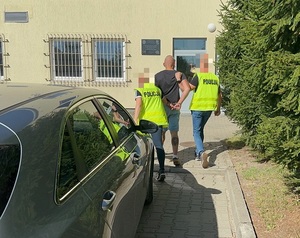 Zatrzymany mężczyzna prowadzony przez policjantów do budynku komendy