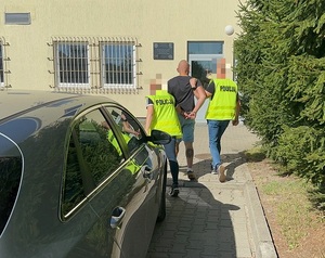 Zatrzymany mężczyzna prowadzony przez policjantów do budynku komendy