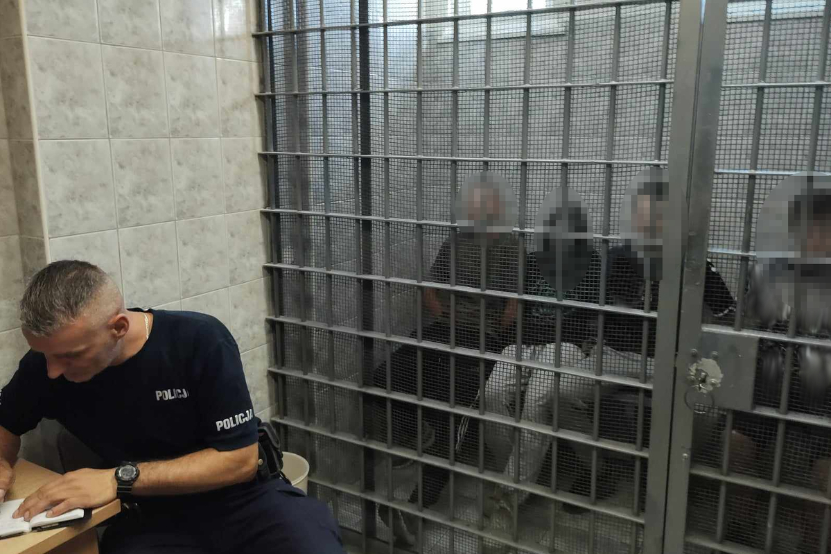 Zatrzymane osoby w policyjnej celi i siedzący przed celą policjant