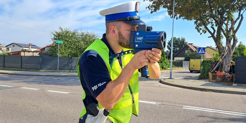 Zdjęcie przedstawia policjanta z ręcznikiem miernikiem prędkości na drodze.