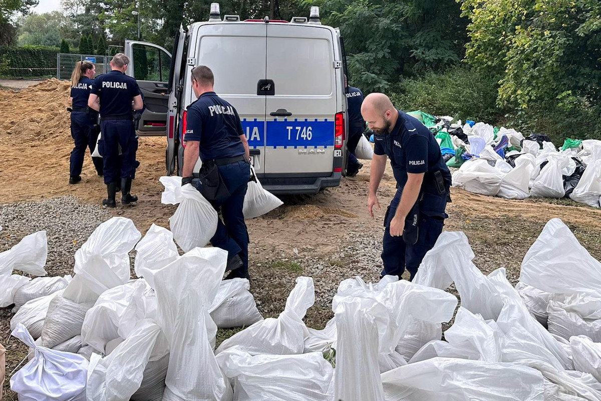 Policjanci pakujący i noszący worki z piaskiem