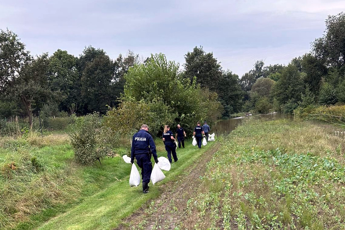 Policjanci pakujący i noszący worki z piaskiem