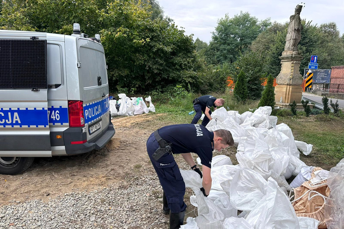 Policjanci pakujący i noszący worki z piaskiem