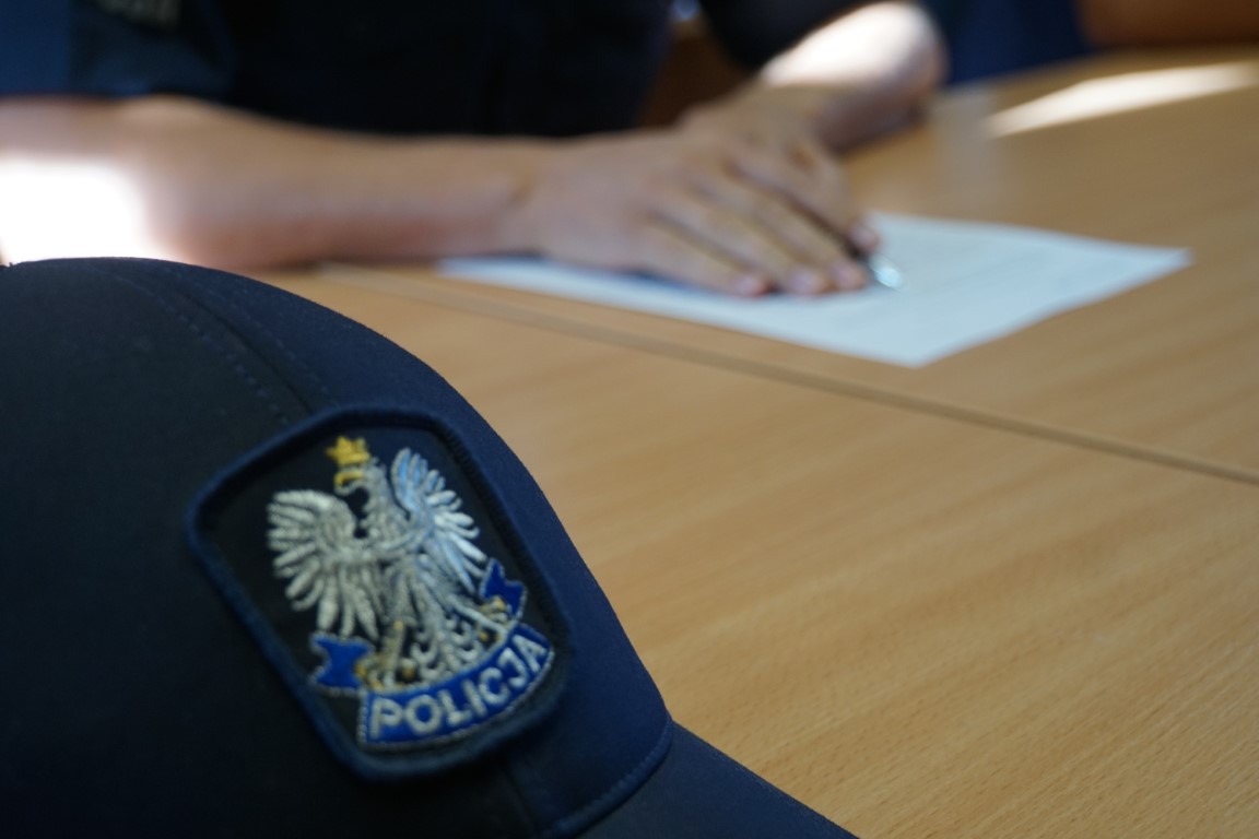 Zdjęcie przedstawia policyjną czapkę oraz fragment policjanta rozwiązujący test.