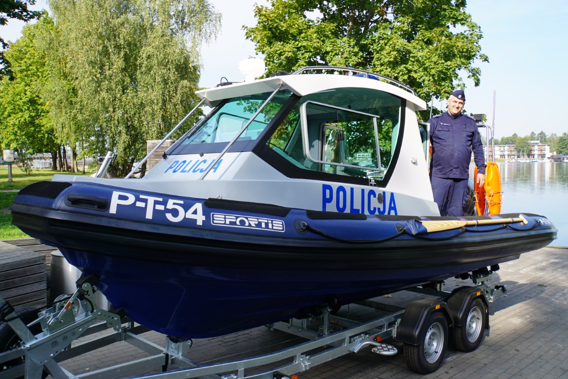 Zdjęcie przedstawia policyjną łódź i umundurowanego policjanta.