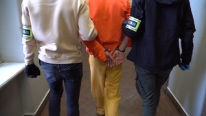 Zdjęcie przedstawia policjantów prowadzących zatrzymanego mężczyznę.