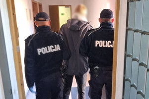 Zdjęcie przedstawia zatrzymanego mężczyznę i umundurowanych policjantów.