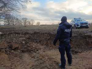 Policjant i radiowóz na miejscu zabezpieczenia niewybuchu.