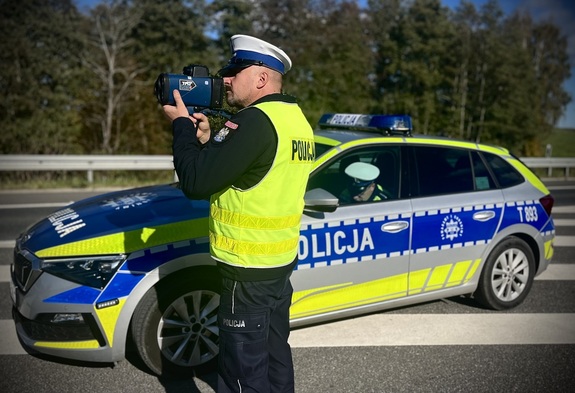 Policjant na tle radiowozu kontrolujący prędkość.