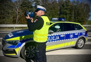 Policjant na tle radiowozu kontrolujący prędkość.