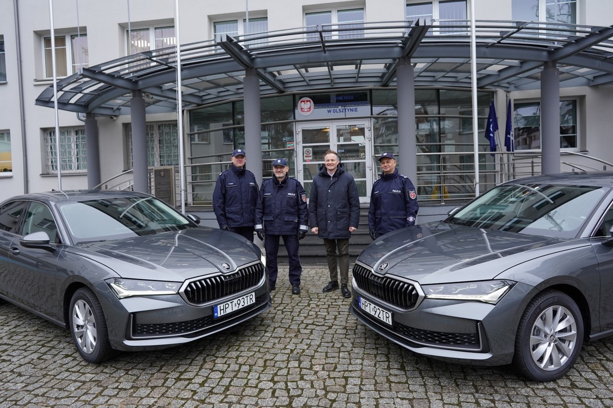 Policyjne radiowozy na tle budynku Komendy Wojewódzkiej Policji w Olsztynie. Na zdjęciu znajduje się: Marcin Kuchciński – Marszałek Województwa Warmińsko-Mazurskiego, insp. Mirosław Elszkowski Komendant Wojewódzki Policji w Olsztynie, insp. Jarosław Brzozowski I Zastępca Komendanta Wojewódzkiego Policji w Olsztynie, podinsp. Rafał Wróbel p.o. Naczelnika Wydziału Transportu KWP w Olsztynie.