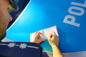 Zdjęcie przedstawia policjanta wypisującego mandat.