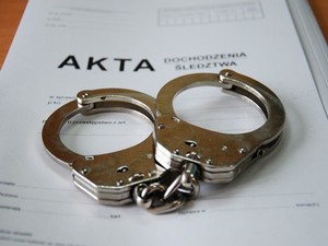 Zdjęcie przedstawia kajdanki i białą teczkę.