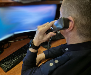 Policjant przy biurku rozmawia przez telefon.
