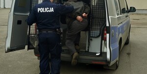 Zatrzymany mężczyzna wsiadający do radiowozu.