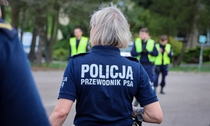 Policjanci w trakcie akcji poszukiwawczej. Na pierwszym planie odwrócona tyłem policjantka z napisem: Policja przewodnik psa.