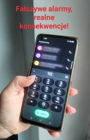 Telefon w ręku i napis "Fałszywy alarm - realne konsekwencje".