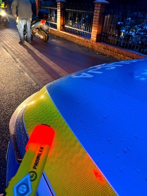 Policyjny radiowóz a w tle motorower i jego kierowca