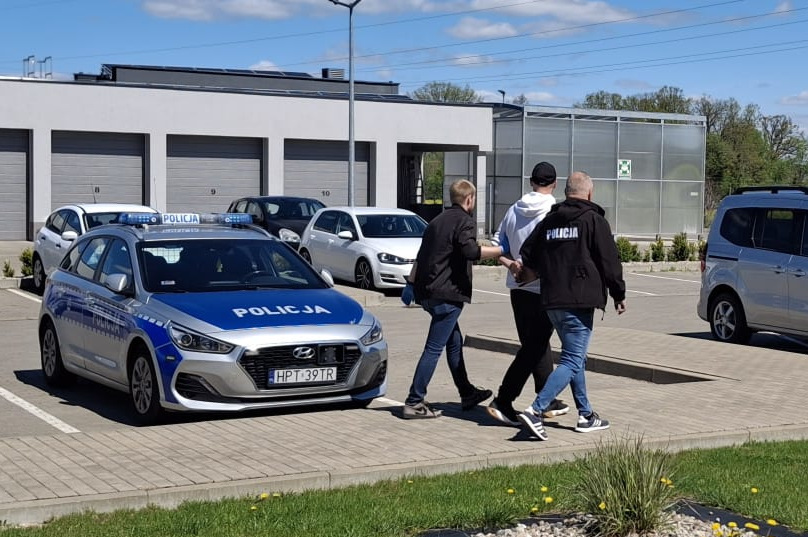 Policjanci prowadzą zatrzymanego mężczyznę do auta