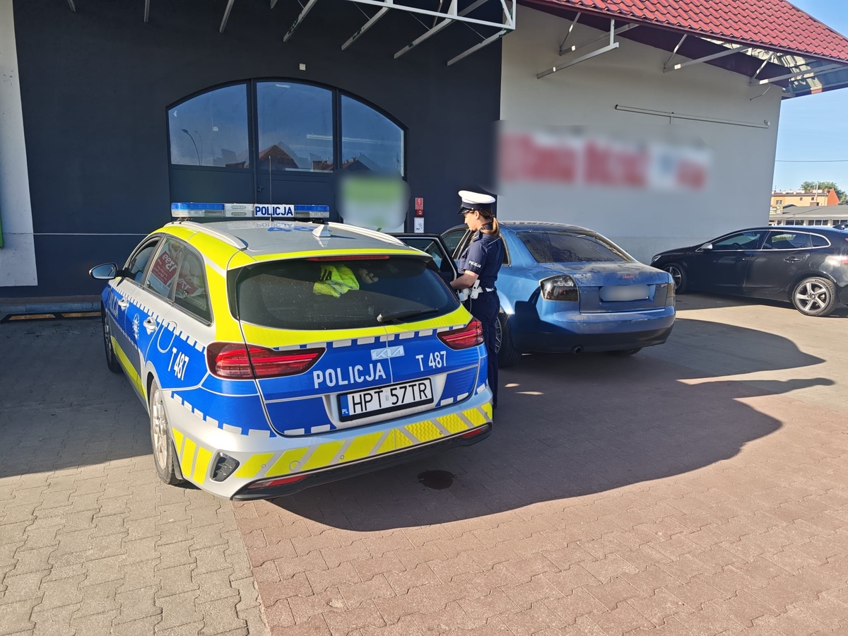 Radiowóz policji oraz policjantka stojąca przy nim