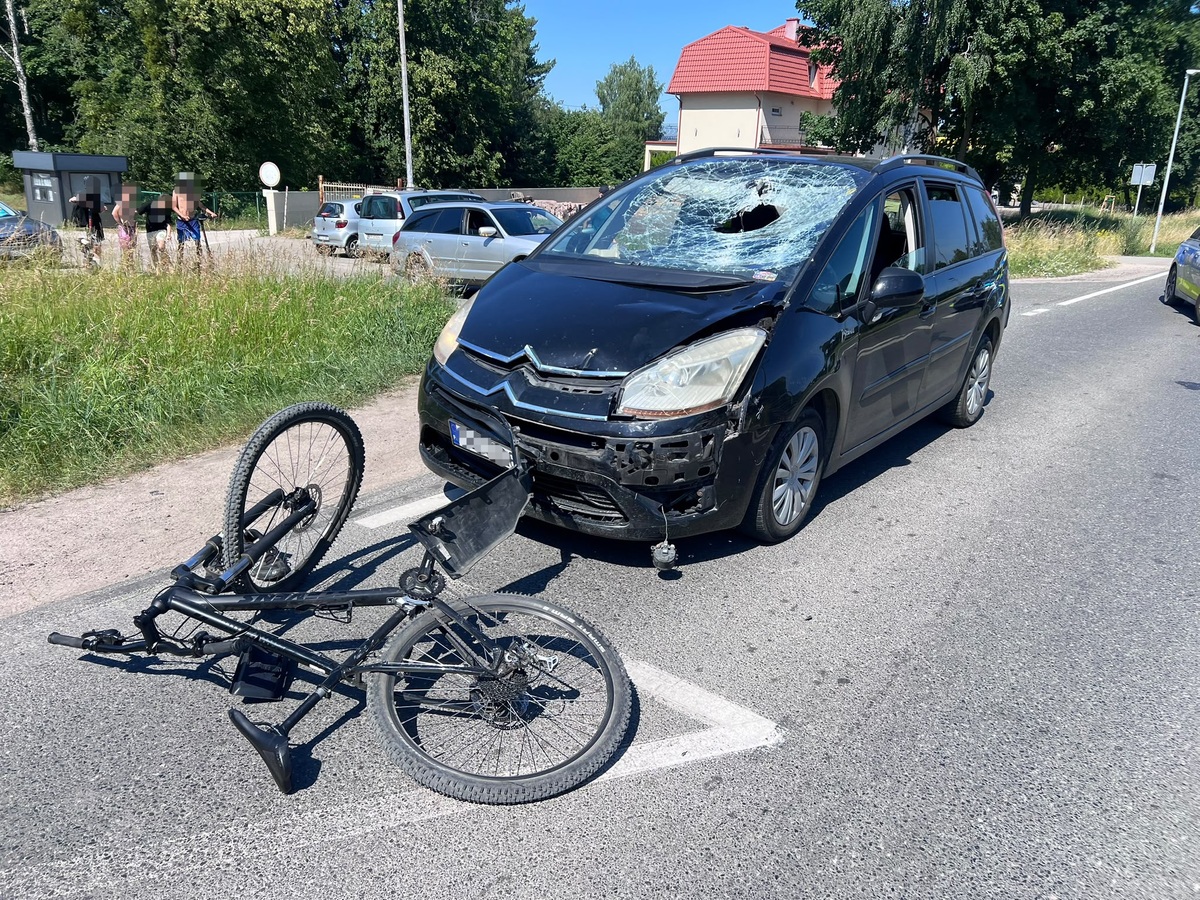 Miejsce zdarzenia drogowego, na pierwszym planie uszkodzony rower, za nim samochód osobowy z uszkodzoną szybą czołową